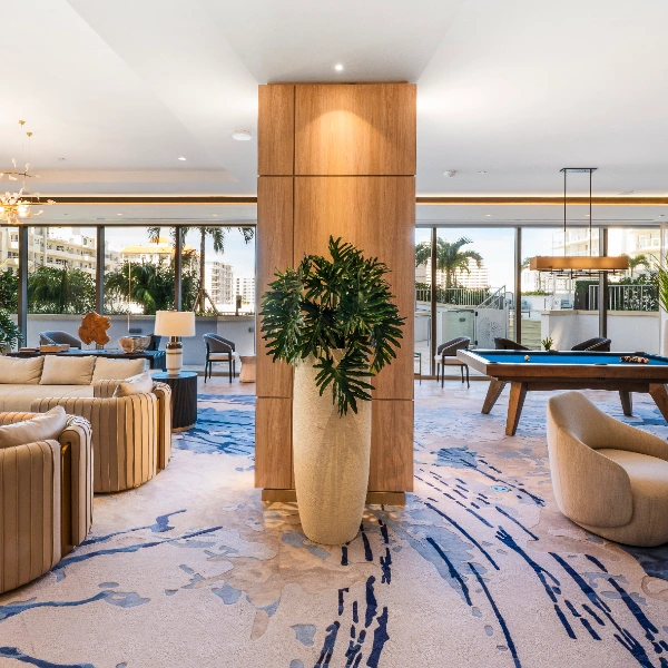 Modern lounge with soft seating, large plants, a central wood column, and a blue-felt billiards table.